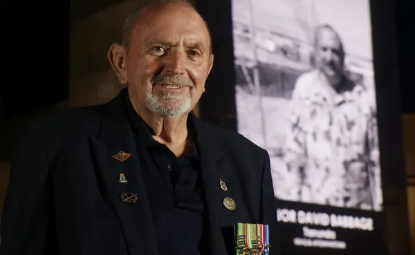 Army veteran standing in front of an illumination depicting himself in uniform on a building