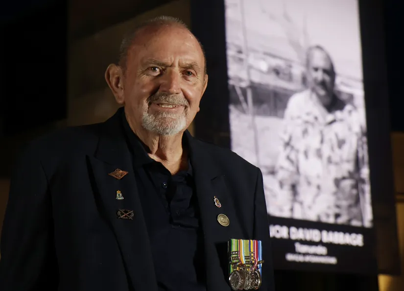 Army veteran standing in front of an illumination depicting himself in uniform on a building