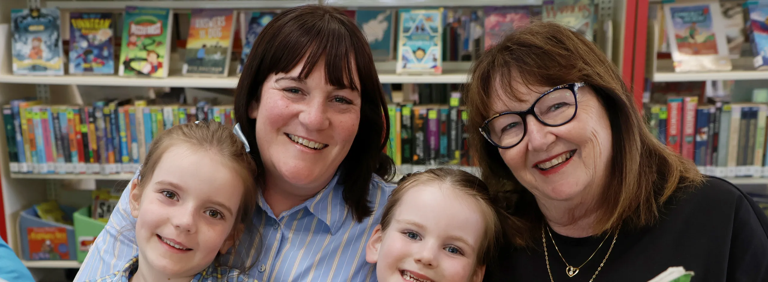 A grandma with her grown up daughter and two grandchildren reading a giant book together in the library