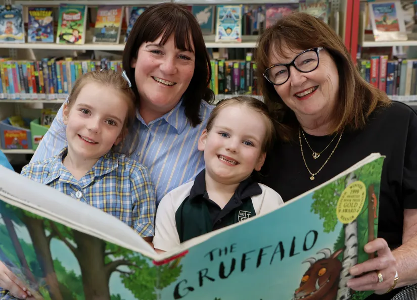 A grandma with her grown up daughter and two grandchildren reading a giant book together in the library