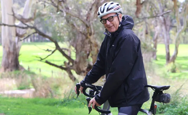 Mayor Bim Lange seated on his bike, wearing helmet and glasses, ready to go for the ride. Large gum trees are in the background
