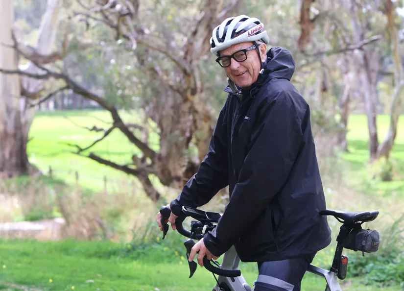 Mayor Bim Lange seated on his bike, wearing helmet and glasses, ready to go for the ride. Large gum trees are in the background