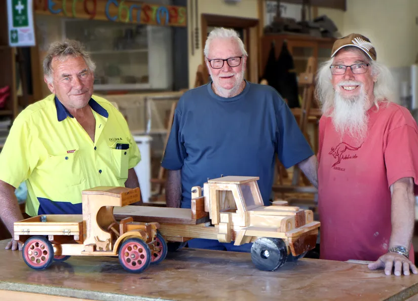 Three men with wooden toys made at the Community Men's Shed