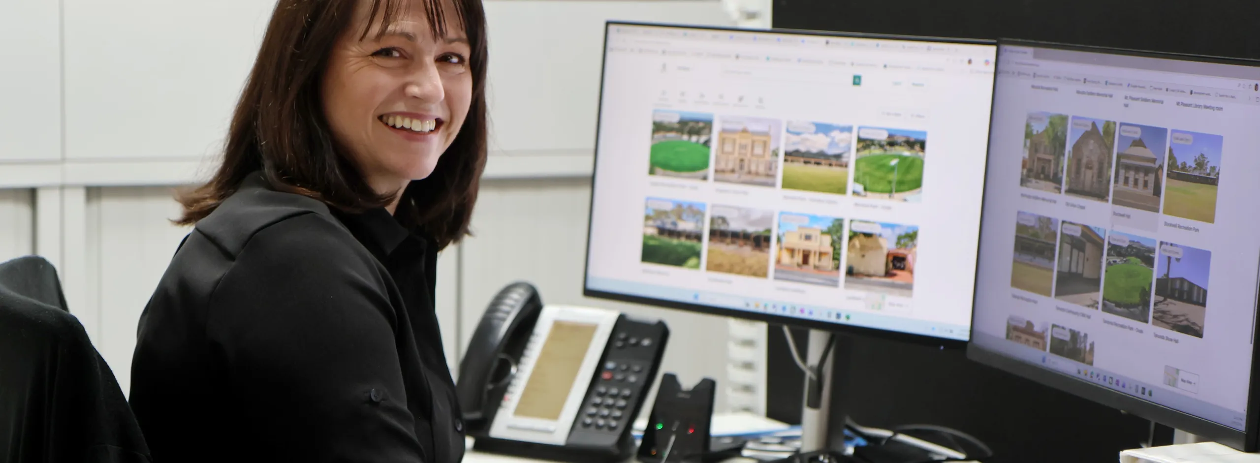 Antonia seated behind a desk with two computer screens showing the Bookable website