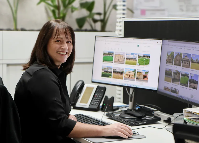 Antonia seated behind a desk with two computer screens showing the Bookable website