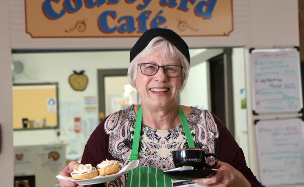 Volunteer cafe assistant holding a cup and plate of scones