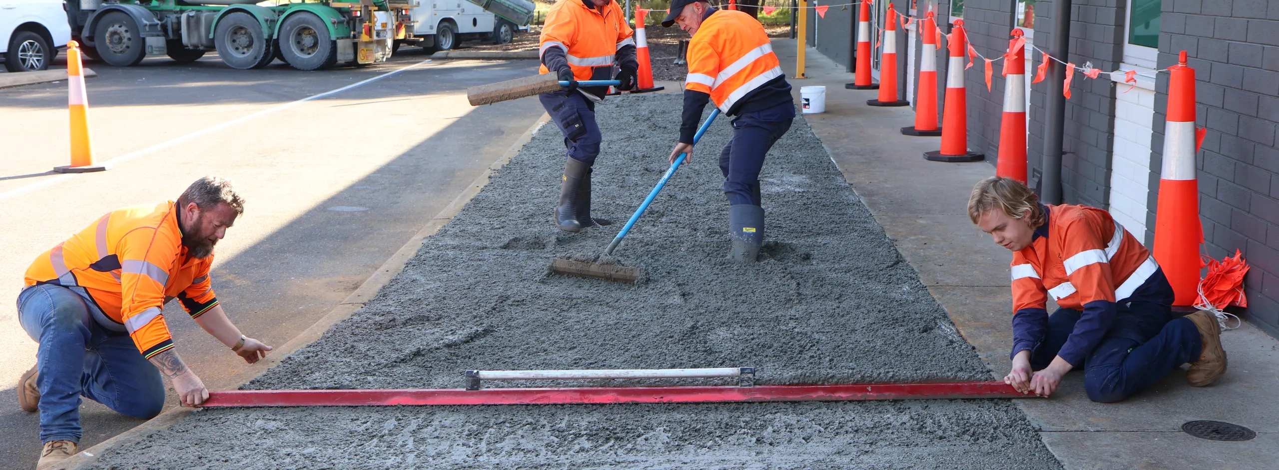 Four council workers installing concrete slab. The cement is still wet and the workers are smoothing the surface with levels and shovels