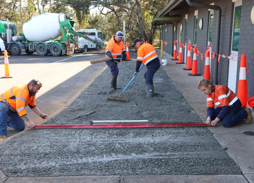 Four council workers installing concrete slab. The cement is still wet and the workers are smoothing the surface with levels and shovels