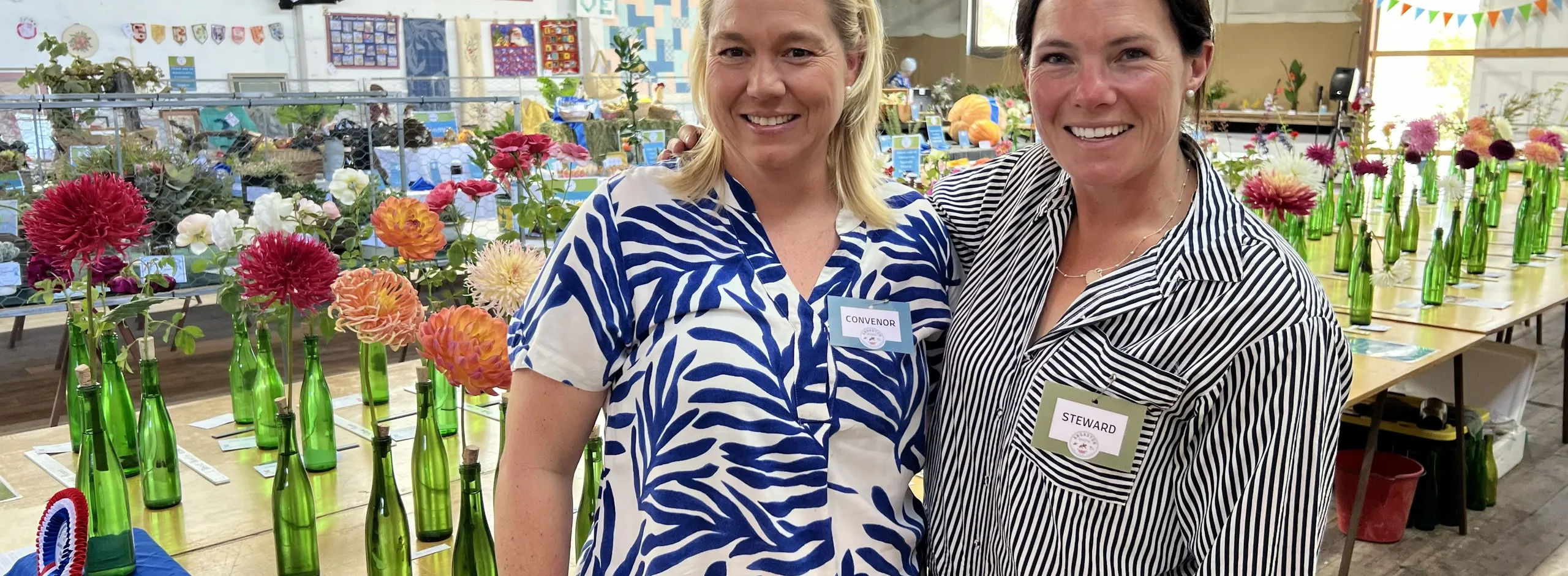 Two women standing in front of a table filled with Dahlias ready for adjudication