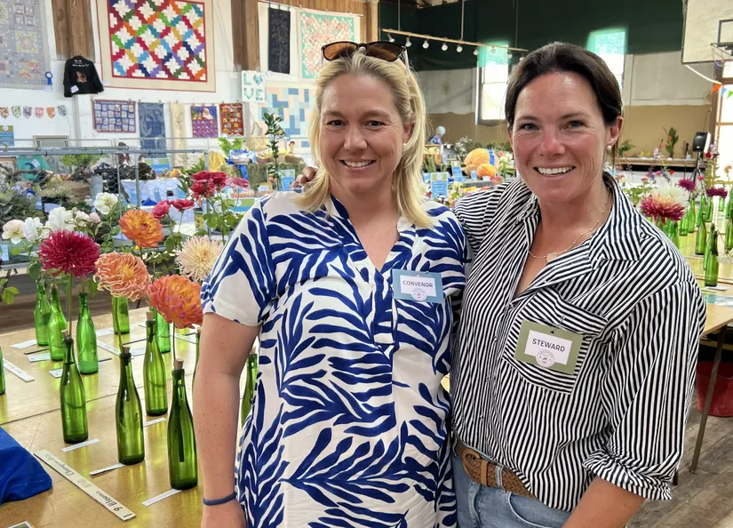 Two women standing in front of a table filled with Dahlias ready for adjudication