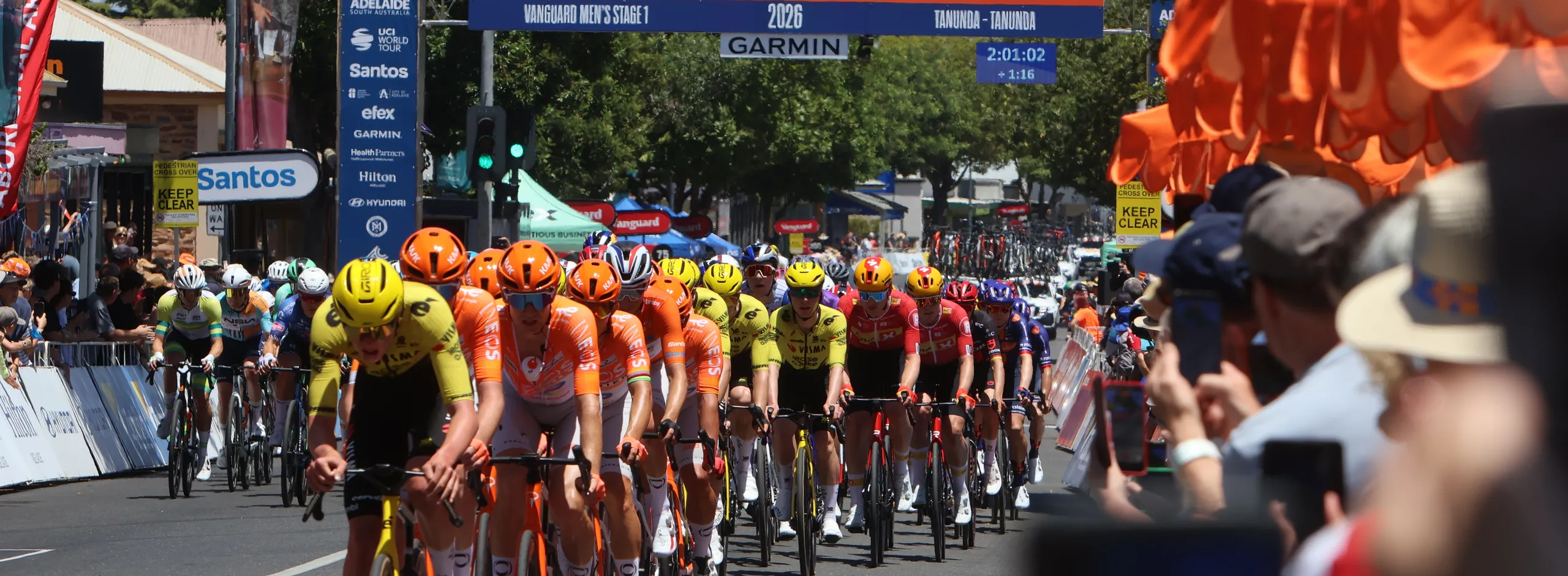 Peloton racing through the main street with crowds cheering and the Tour Down Under archway in the background
