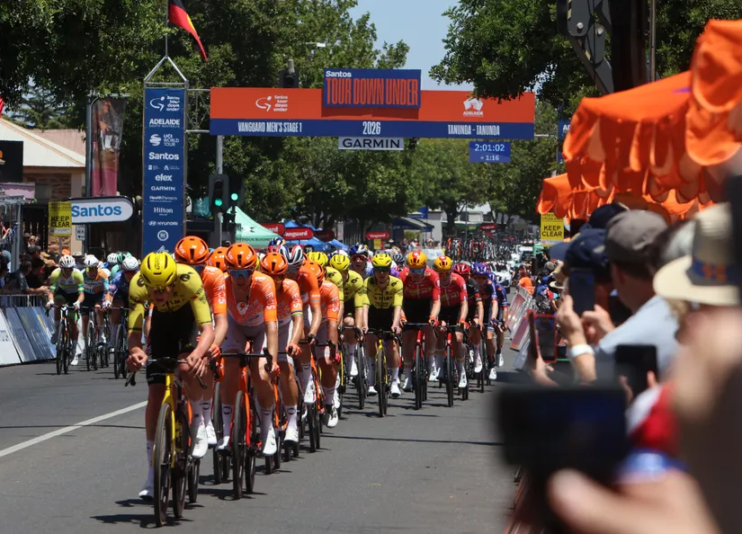 Peloton racing through the main street with crowds cheering and the Tour Down Under archway in the background