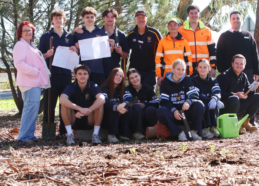 Group of High School students with teachers and staff grouped near a freshly planted out garden bed with plans and watering can.