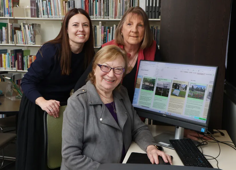 Three women seated around a computer screen which is showing the new online Barossa Cemeteries family research tool that goes live on 27 August.