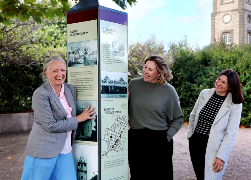 Three women with a heritage sign in the heart of Tanunda